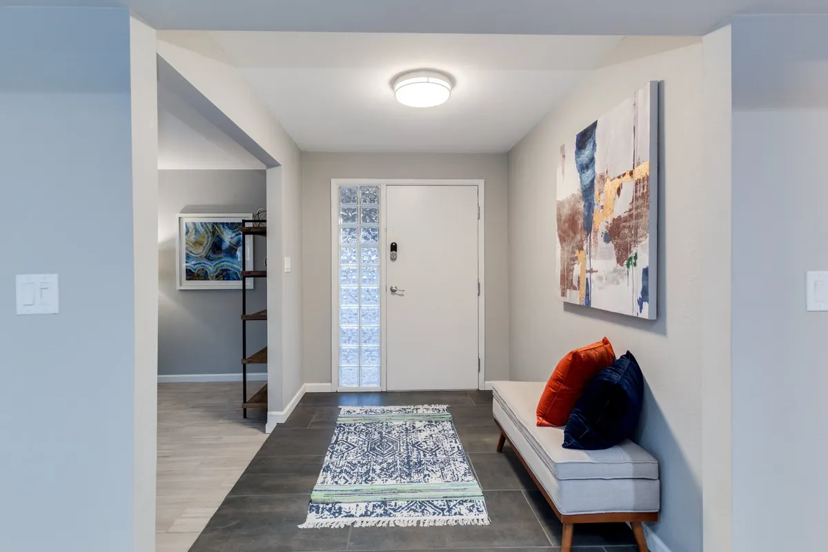 An inviting and serene entryway featuring a decorative rug, tasteful artwork, and a cozy seating area with cushions. The design provides a welcoming first impression, offering a calm and peaceful transition from the outside world into the home.