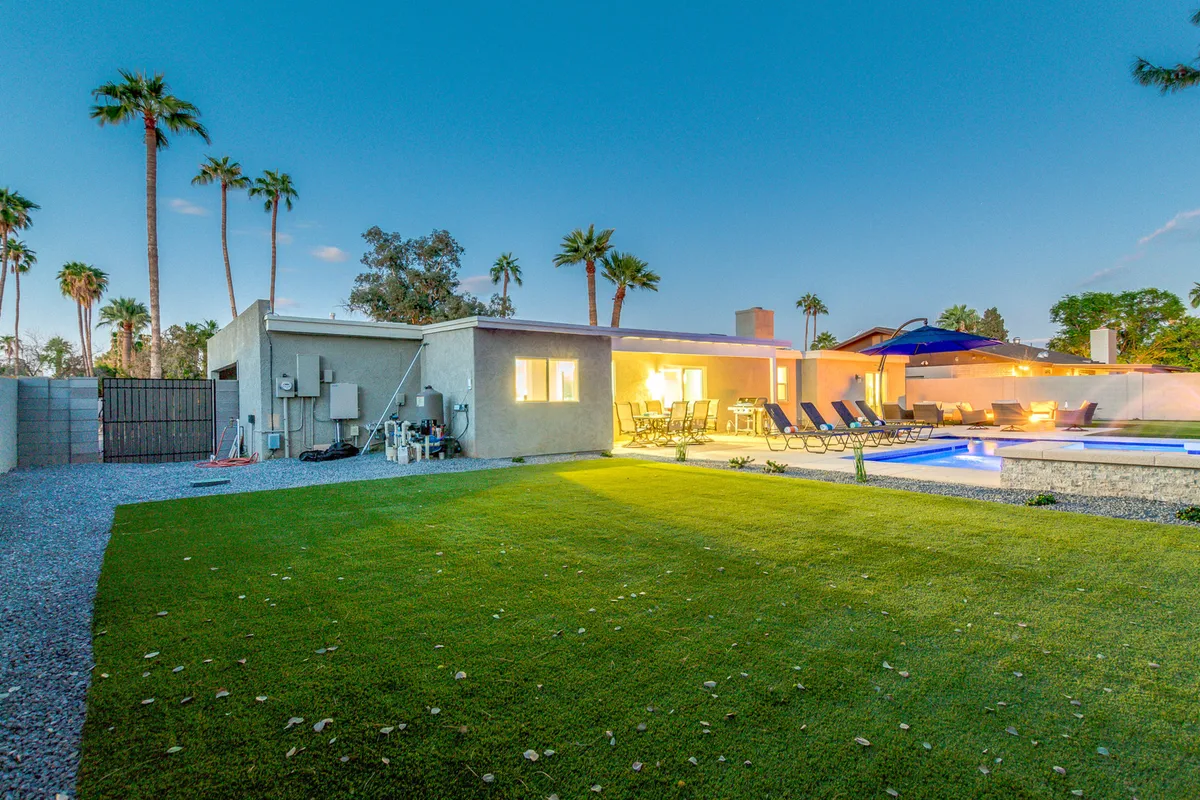 A cheerful exterior with a sparkling swimming pool, ample outdoor seating, palm trees, and a well-maintained lawn. The scene suggests a relaxed environment perfect for sunbathing, casual outdoor dining, and socializing under the sun or stars.