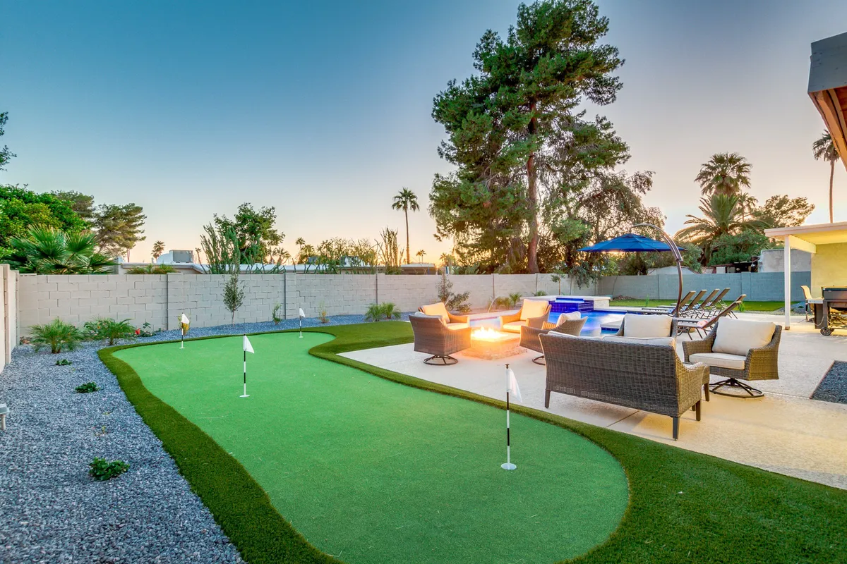 A backyard view highlighting the putting green, cozy fire pit surrounded by seating, and the pool in the background. The scene invites guests to enjoy recreational activities or unwind by the fire as the sun sets.