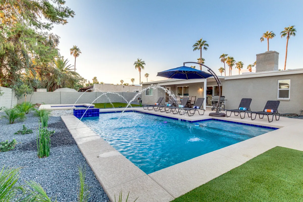 A sun-drenched swimming pool with fountain jets, surrounded by lounge chairs, an umbrella, and swaying palm trees. The setting radiates a leisurely and cheerful mood, inviting guests for a refreshing dip, sunbathing, or unwinding with friends.