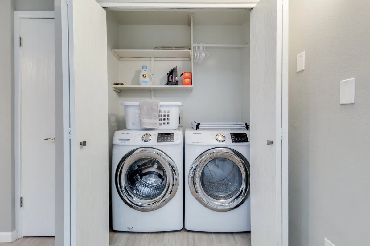 A neat and organized laundry area featuring a washer and dryer unit with ample shelving above for storing laundry supplies. The setup is clean, efficient, and immediately communicates convenience for guests managing laundry during their stay.