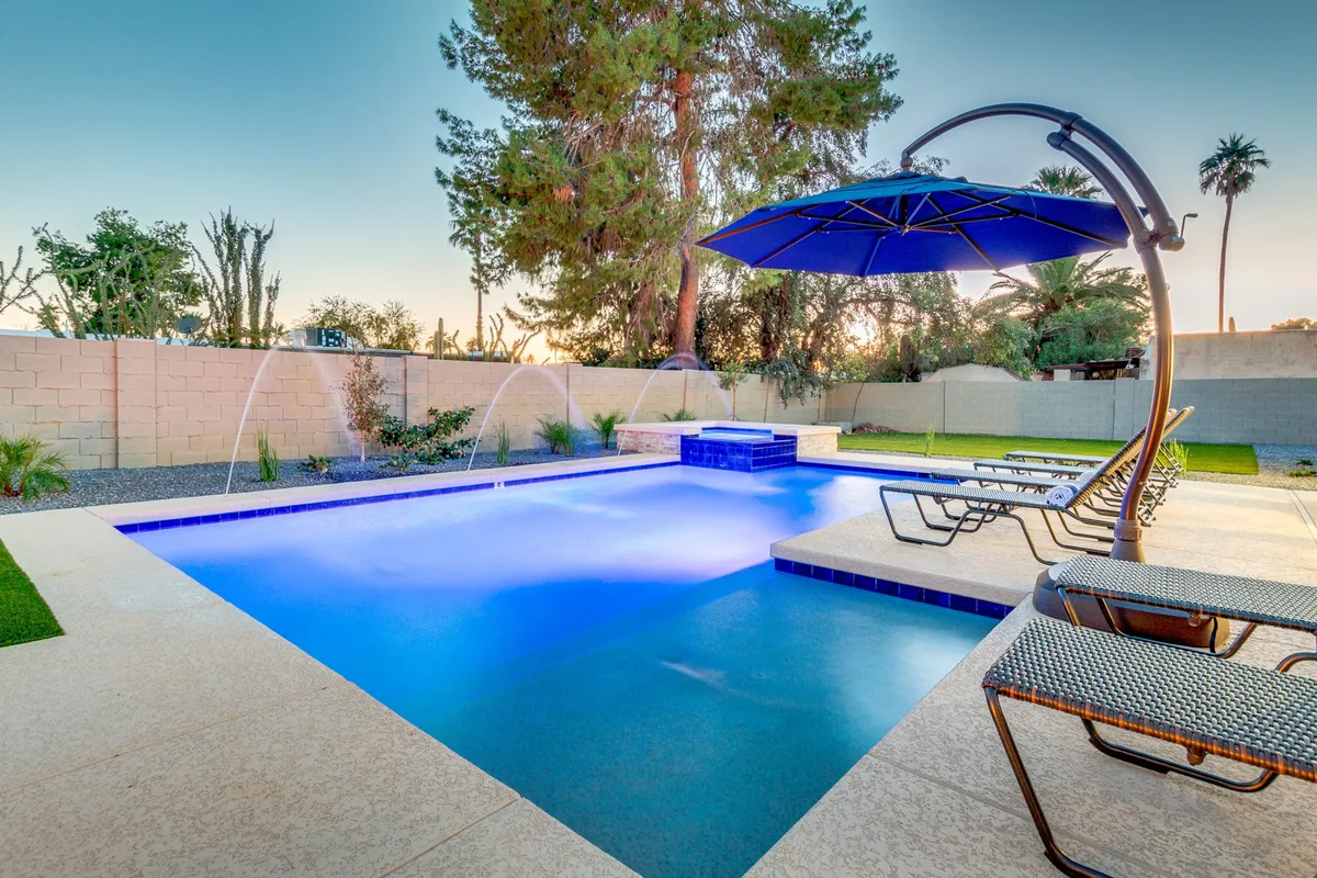 An inviting exterior scene featuring a pristine swimming pool surrounded by blue umbrellas and comfortable lounge chairs. The tranquil setting is highlighted by gentle water features and spaces for both relaxation and social gatherings. Lush landscaping enhances the sense of calm, making it an ideal spot to unwind after a busy day.