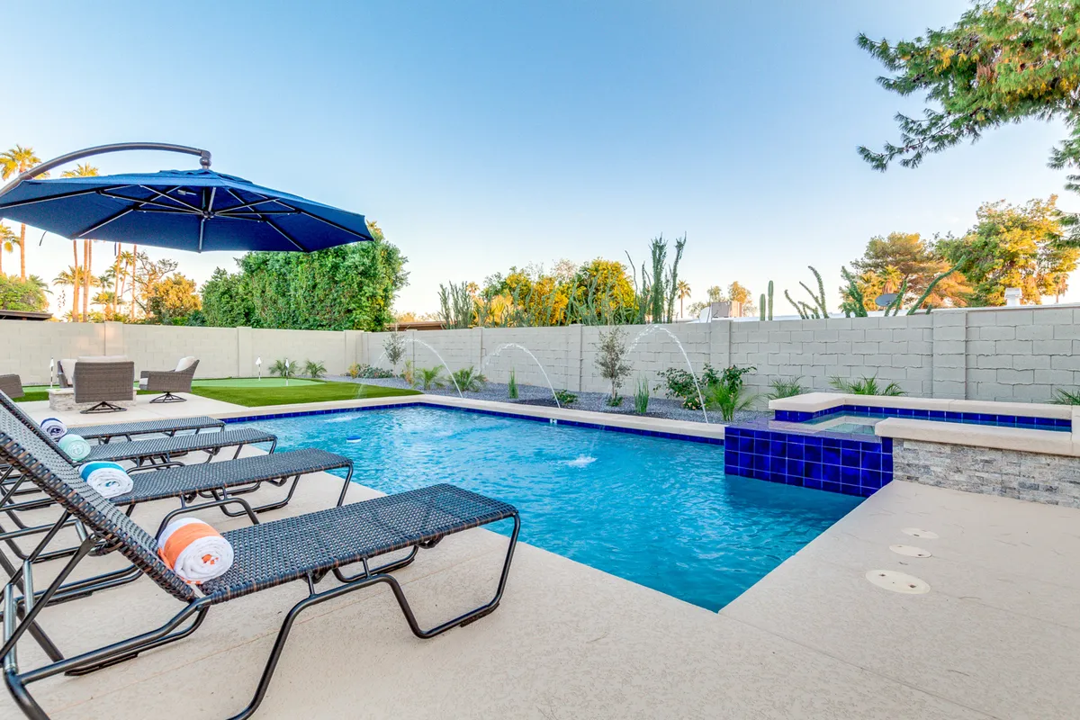 A beautiful shot centered on the swimming pool bordered by lounge chairs and umbrellas, with lush green landscaping and water features that add to the tranquil ambiance. The space feels open and inviting, perfect for sunbathing or casual gatherings.