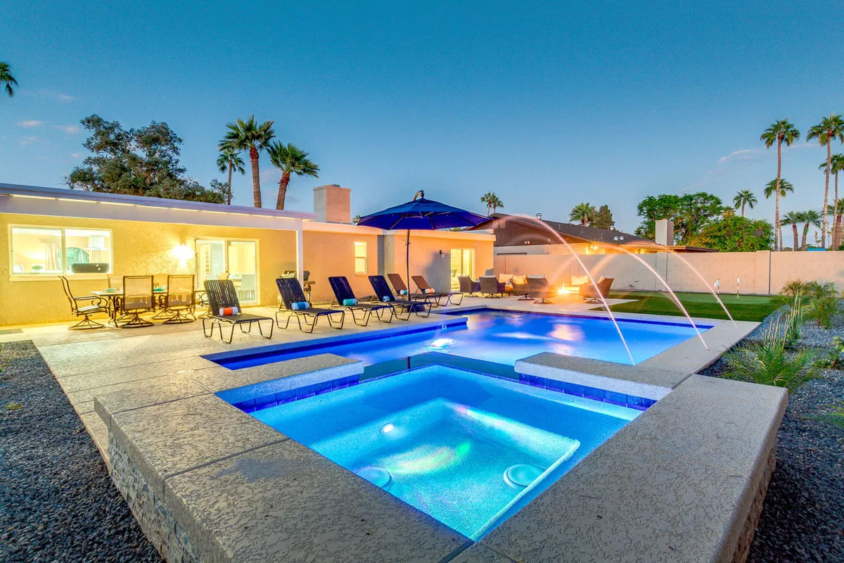 This inviting backyard view displays a heated swimming pool, attached hot tub, comfortable outdoor seating, and attractive landscaping. Warm lighting hints at sunset, inviting relaxation and evening social gatherings for families.
