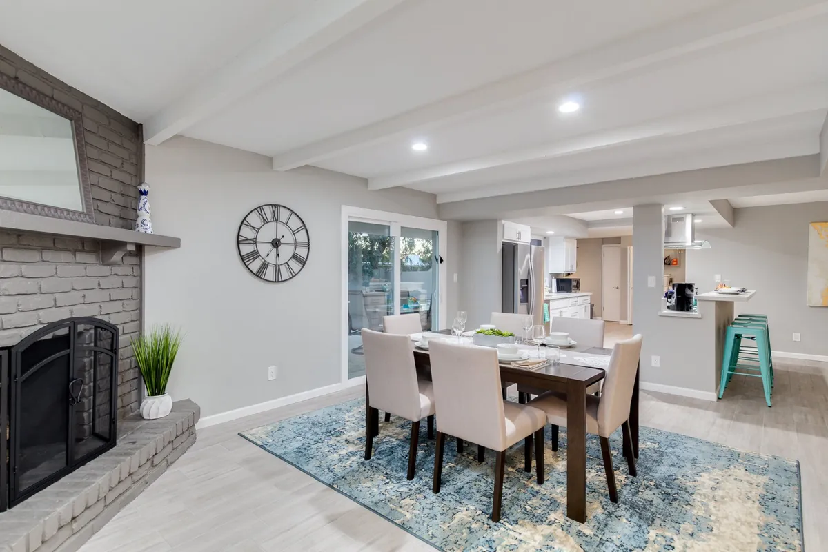 This image captures the dining area with its elegant table, a glowing fireplace, large windows for natural light, and decor accents like a prominent clock. The scene exudes warmth and is staged for hosting memorable dinners and relaxed evenings by the fire.