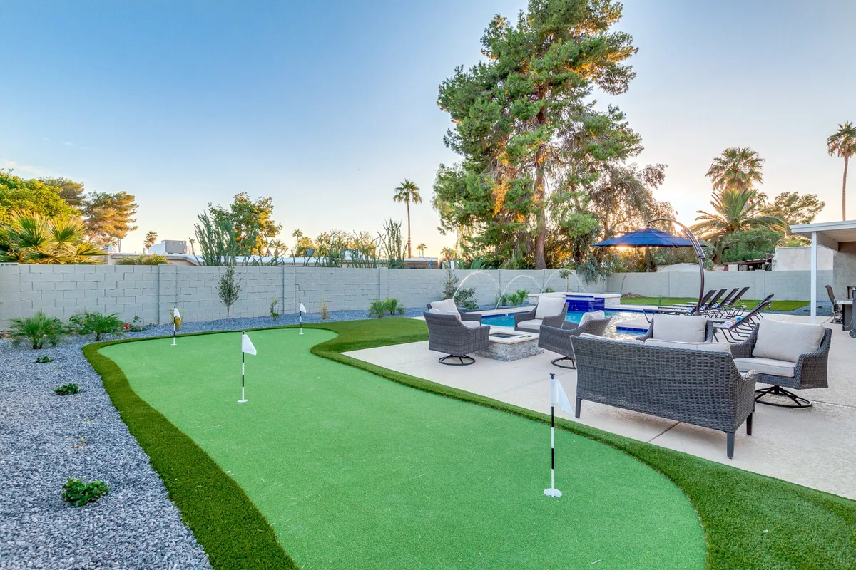 The hero image showcases a stunning backyard oasis featuring a sparkling heated swimming pool, a lush putting green for friendly golf matches, comfortable outdoor seating, tall palm trees, and elegant decorative stones, all bathed in the warm glow of a Scottsdale sunset.