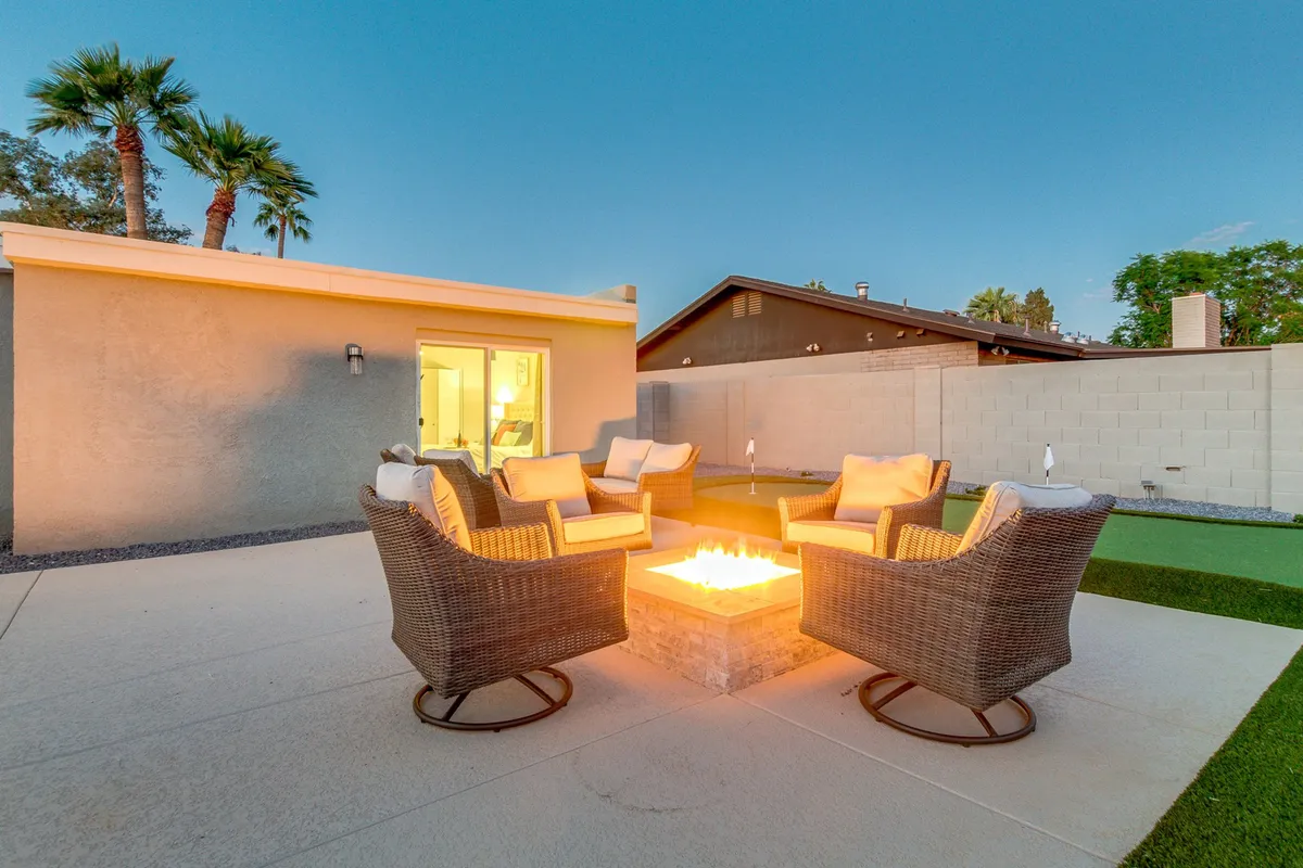 A cozy outdoor fire pit surrounded by comfortable seating and lush landscaping, perfect for gathering with friends in the evening. The warm glow of the fire creates a welcoming ambiance as twilight falls, inviting guests to relax and socialize before a night out.