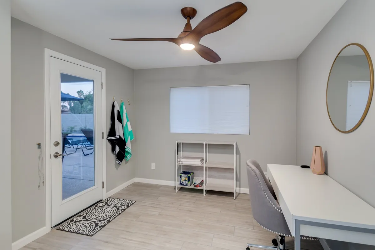 An inviting interior scene with a desk and chair arranged near a circular mirror and ceiling fan, with a door that appears to lead directly outside. The design feels functional yet welcoming, suggesting seamless transitions between work, relaxation, and coming or going.