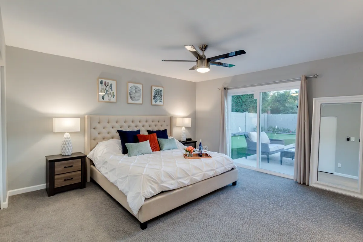 A serene bedroom with a neatly made bed, decorative pillows, nightstands on each side, and a sliding glass door filling the room with soft, natural light. The decor is minimalist and calming, perfect for restful nights.