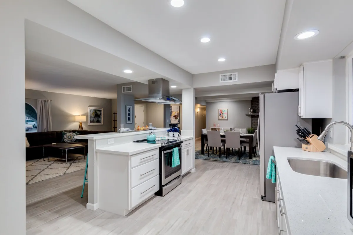 This image showcases the open-concept layout featuring the kitchen island, stainless steel appliances, dining area, and living room—all in one cohesive space. The view highlights the seamless flow between the chef’s kitchen and the great room, emphasizing the heart-of-the-home atmosphere and communal energy described in the section.